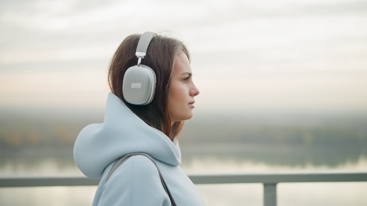 Close-up side view of girl walking majestically, focused and listening to music with headphones, iron rail in background, serene atmosphere, peaceful outdoor stroll in nature, urban setting