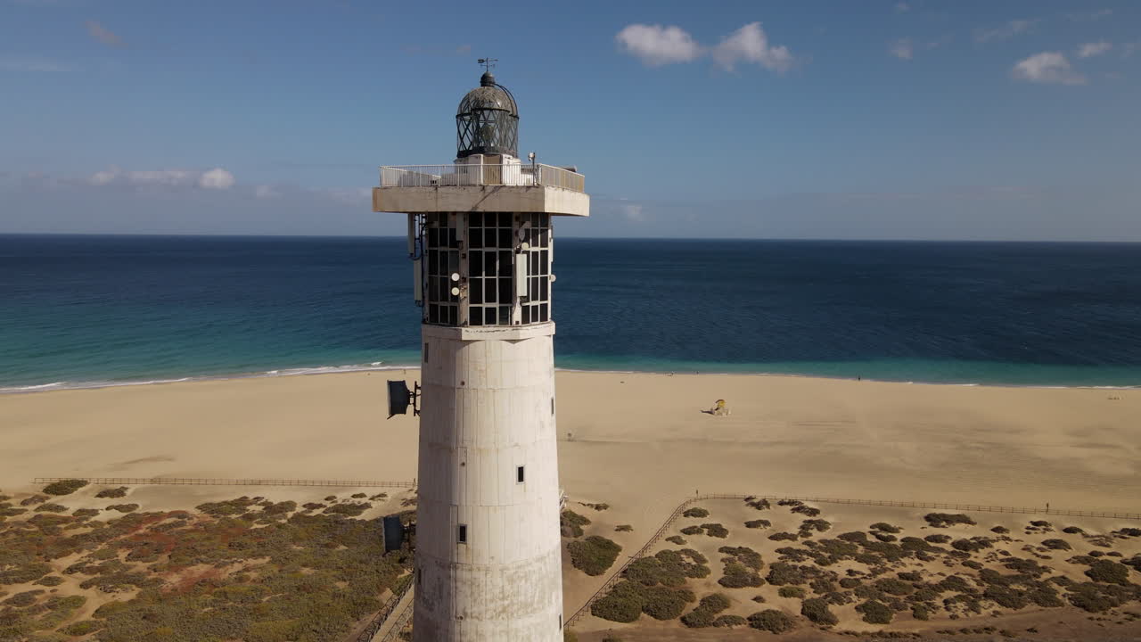 toma aerea en orbita ya poca distancia del faro de morro jable, con la hermosa playa del mismo nombre apareciendo al fondo
