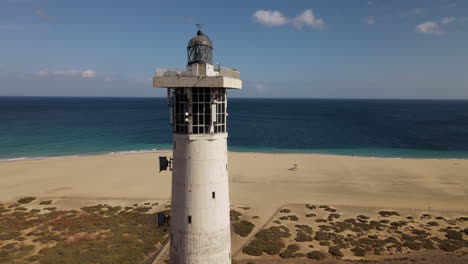 Toma-Aérea-En-órbita-Ya-Poca-Distancia-Del-Faro-De-Morro-Jable,-Con-La-Hermosa-Playa-Del-Mismo-Nombre-Al-Fondo