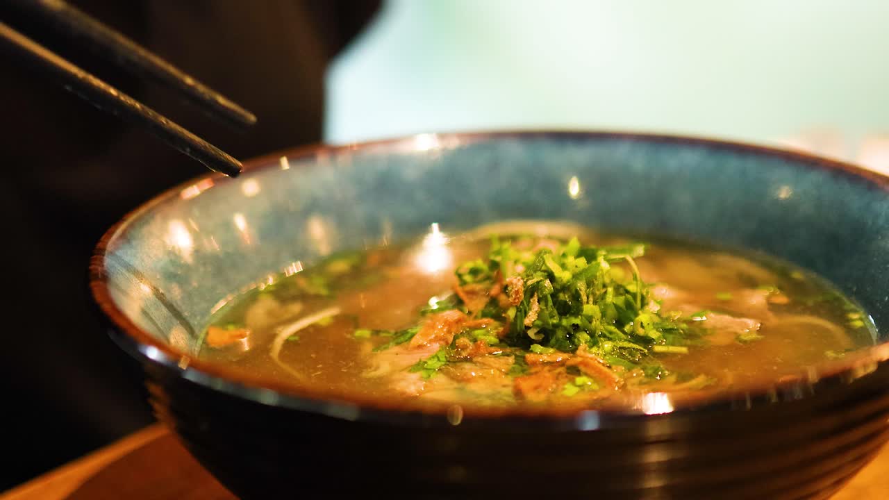 Chopsticks lift tender beef from a steaming bowl of Vietnamese pho, highlighting fresh herbs and rich broth