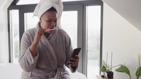 mujer afroamericana de talla grande cepillándose los dientes y usando un teléfono inteligente, sin alteración, cámara lenta