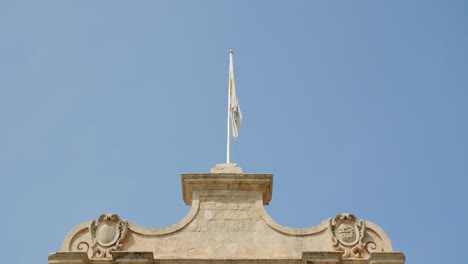 flag of mdina waving on top of city gate in malta against clear blue sky