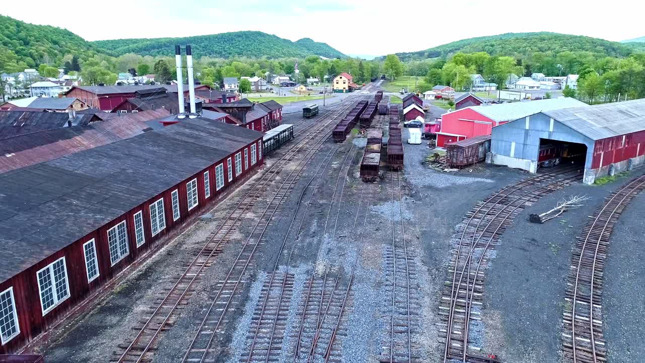 una vista aérea de una carretera ferroviaria de carbón de vía estrecha abandonada con tolvas oxidadas y vagones de carga y un edificio de apoyo que comienza a restaurarse