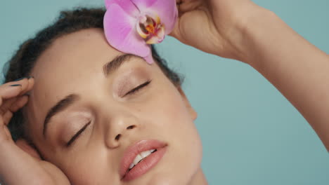 retrato de belleza de cerca hermosa mujer tocando el rostro con colorida flor de orquídea rosa acariciando suave piel sana tez disfrutando de fresca fragancia natural concepto de cuidado de la piel