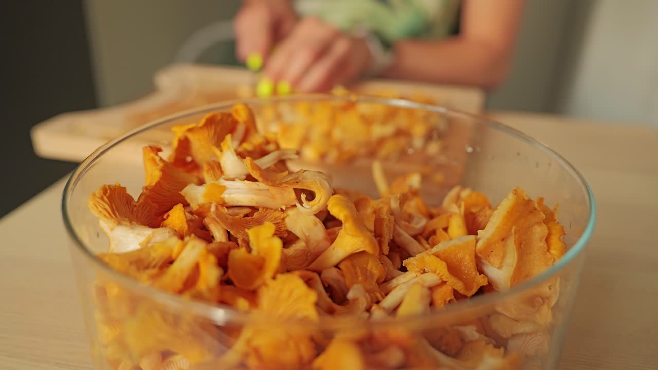 Focused glass bowl with fresh chanterelles, cooking action behind in soft light