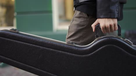 hombre caminando con un caso de guitarra en la calle