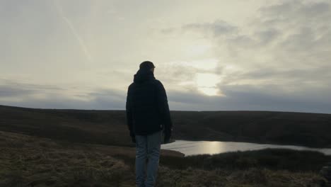 Young-boy-standing-and-looking-out-on-to-the-winter-landscape,-with-moorlands,-fens,-a-lake-and-stormy-winters-sky