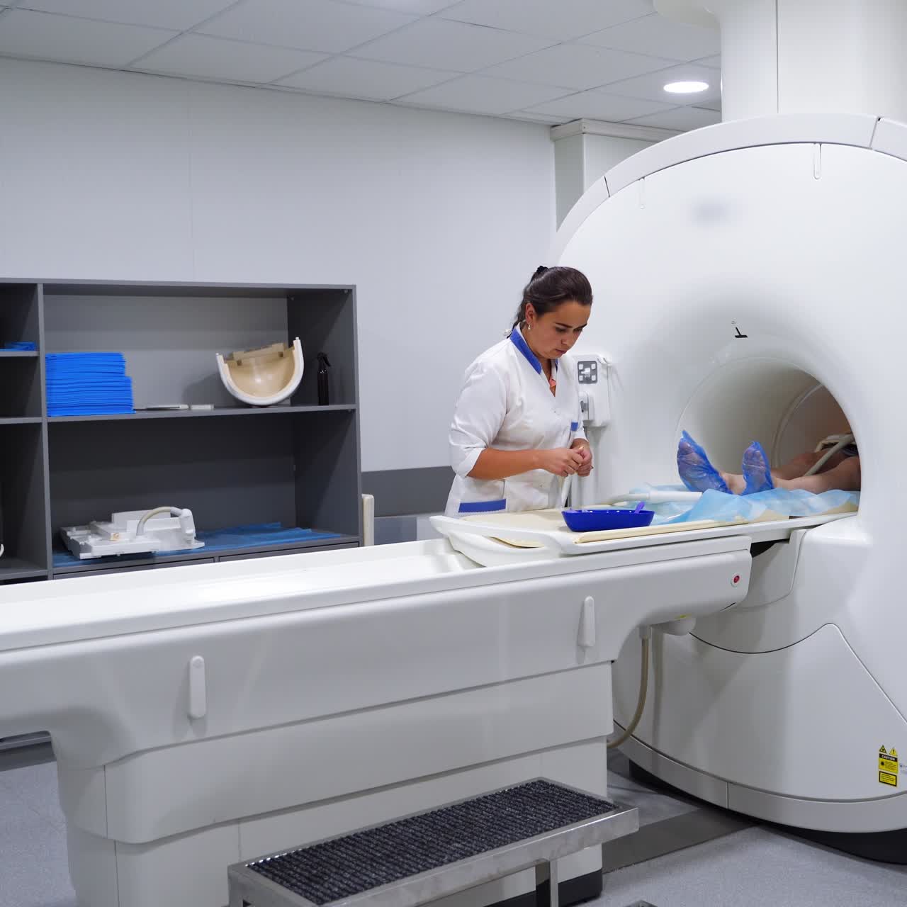 Un medico in piedi vicino a uno scanner per risonanza magnetica (MRI) che prepara gli strumenti. Il paziente è sdraiato all'interno della macchina