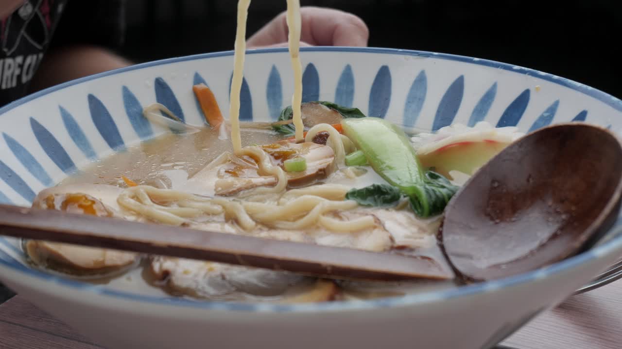 Tonkotsu ramen bowl with char siu pork and fresh vegetables being garnished with greens
