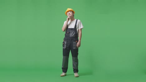 full body of asian man worker wearing goggles and safety helmet thinking and looking around then raising his index finger while standing in the green screen background studio