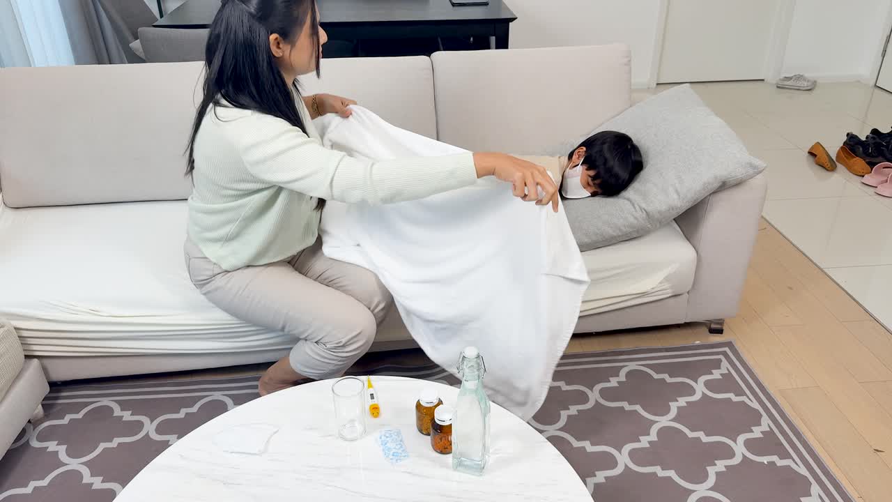 Mother gently covers sick child with blanket in bright living room, nurturing and comforting atmosphere