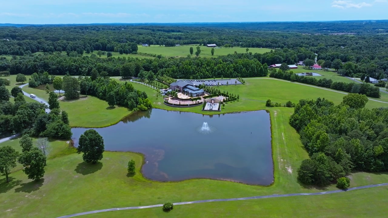 Elegant bryllupssted med springvandsdam ligger midt i grønne græsgange nær Trenton, Georgia, træomkranset grusindkørsel snor sig gennem tæt skov og åbne marker. Bredt luftfoto med drone