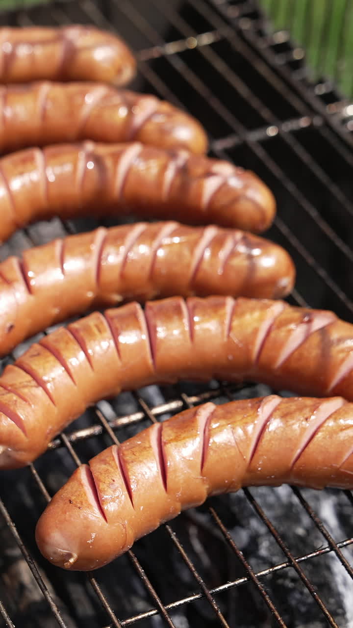 Hot dog sausages roasting in smoke. Chef opens grill grate and turns over juicy sausages. Delicious food for picnic in summer. Eating in nature. Vertical video