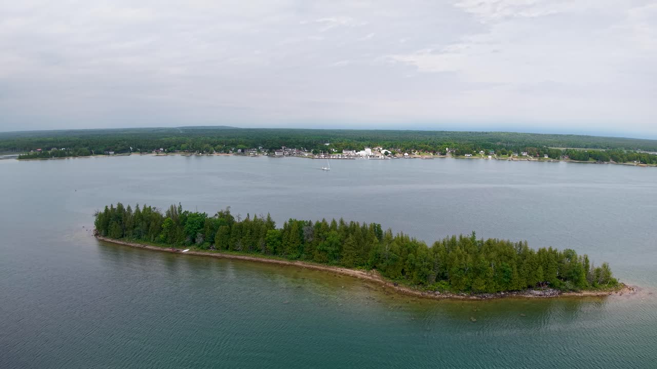 Aerial drone shot of a small forested island surrounded by calm blue water in a vast open lake