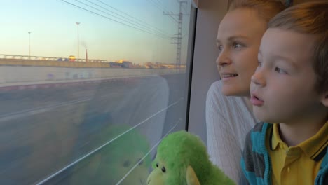 small boy with mother sitting against window in their rail train place and watching outside