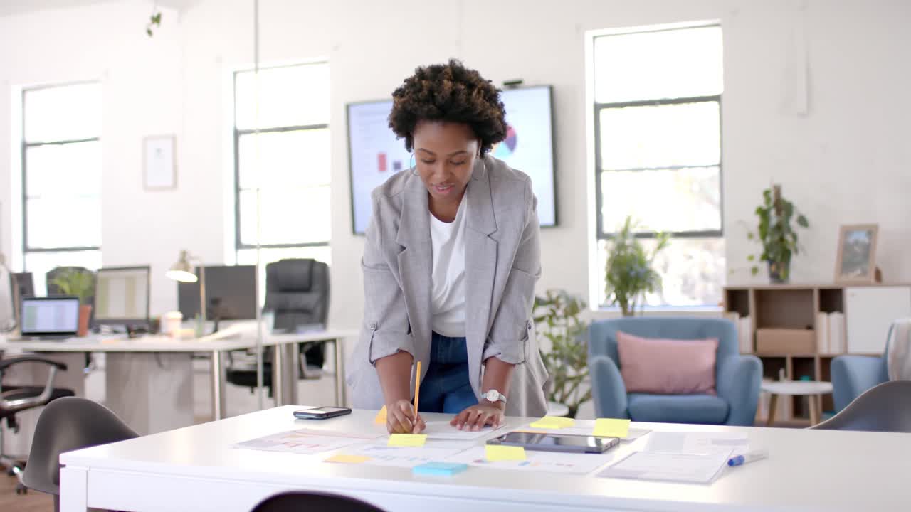 Happy african american casual businesswoman using tablet and taking notes in office, slow motion