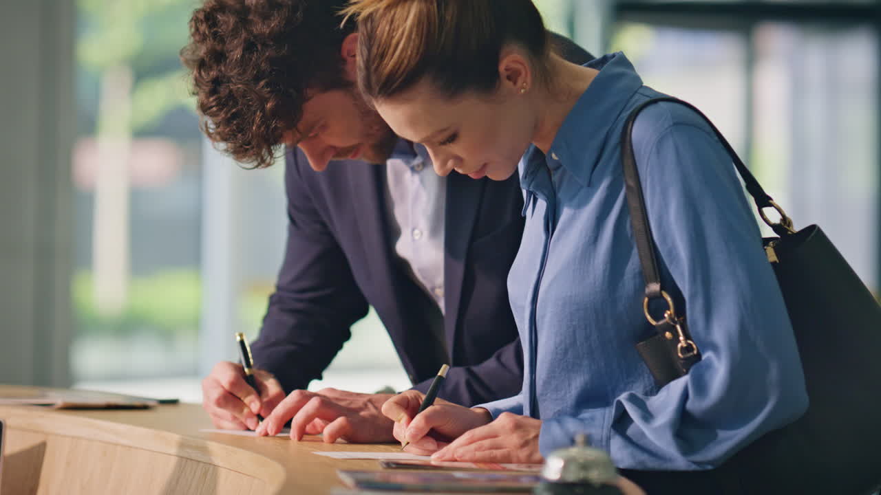 손님들이 카운터 근접에서 호텔 양식을 채우고 있습니다. 웃는 여행 부부는 체크인합니다.