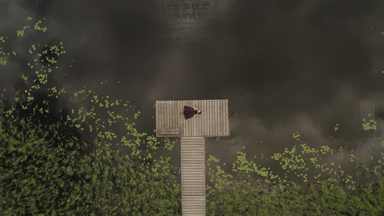 Aerial zoom in on woman resting on a wooden path