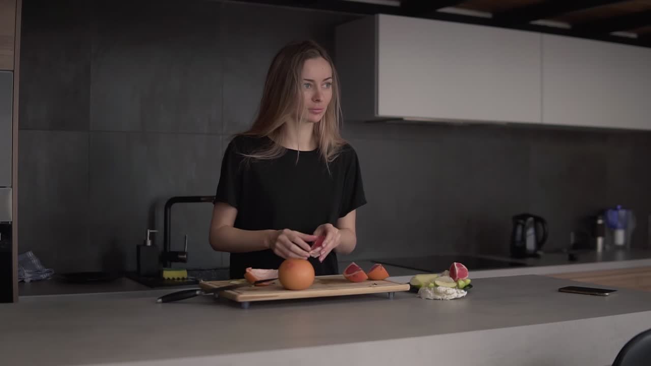 Ritratto di una donna che pulisce la buccia di pompelmo su un tagliere in cucina.
