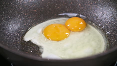 cracking and frying two eggs in a black pan, fried eggs, egg yolk and egg white during cooking process