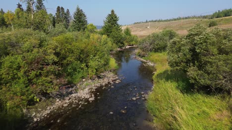 aerial drone tracks natural stream flow along cariboo highway near 127 mile house, british columbia, canada