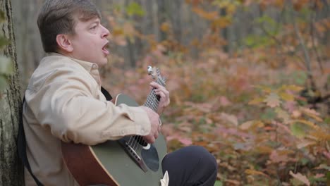 guy playing by the guitar in autumn background with yellow leaves in the park