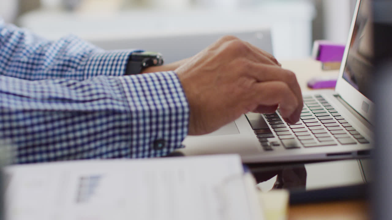 Video of hands of senior biracial man at desk using laptop at home