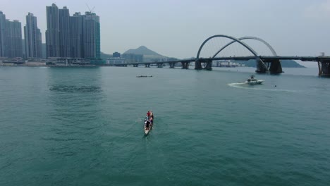 Dragon-Boat-team-rowing-to-the-pace-of-an-onboard-Drummer,-Aerial-view