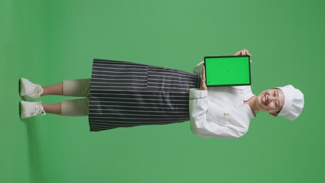 full body of asian woman chef smiling and showing green screen tablet to the camera while standing in the green screen background studio