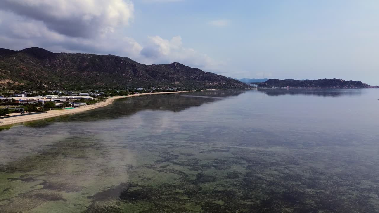 Epic 4K drone shot from the sea facing land, slowly sweeping right-to-left to reveal the beach, houses, and mountain backdrop in Phan Rang, Vietnam.