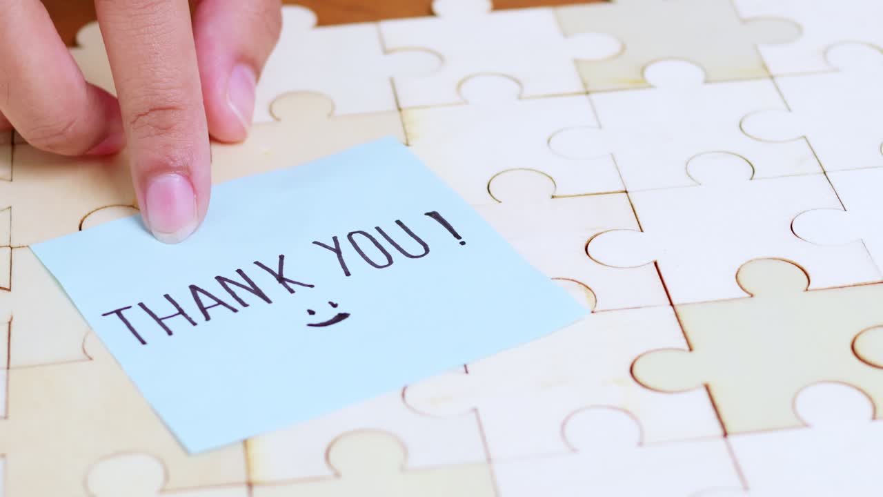 A person's hand places aThank Younote on a puzzle symbolizing appreciation in a cozy workspace