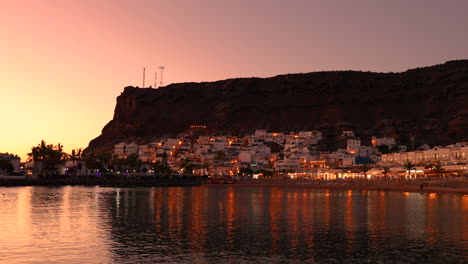 mogan beach during sunset with the city lit up by street lights and freshly lit streets of the grand canary island valley 4k slow motion capture at 60fps
