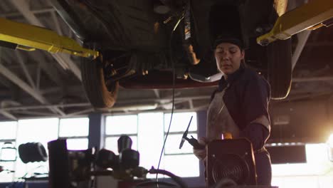 female mechanic wearing welding helmet working under a car at a car service station