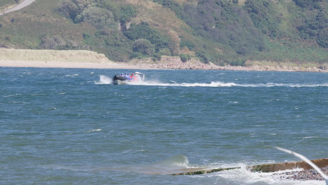 Red speedboat moves swiftly across blue water, distant hills, bright daylight, seagull flies past