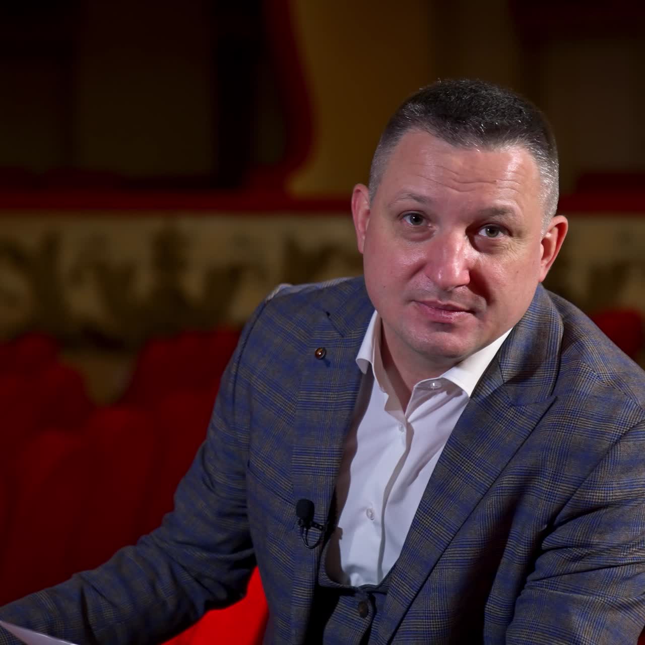Ritratto di un attore durante le prove. Uomo in abito seduto in una sala teatrale che esegue un monologo tenendo in mano un copione.