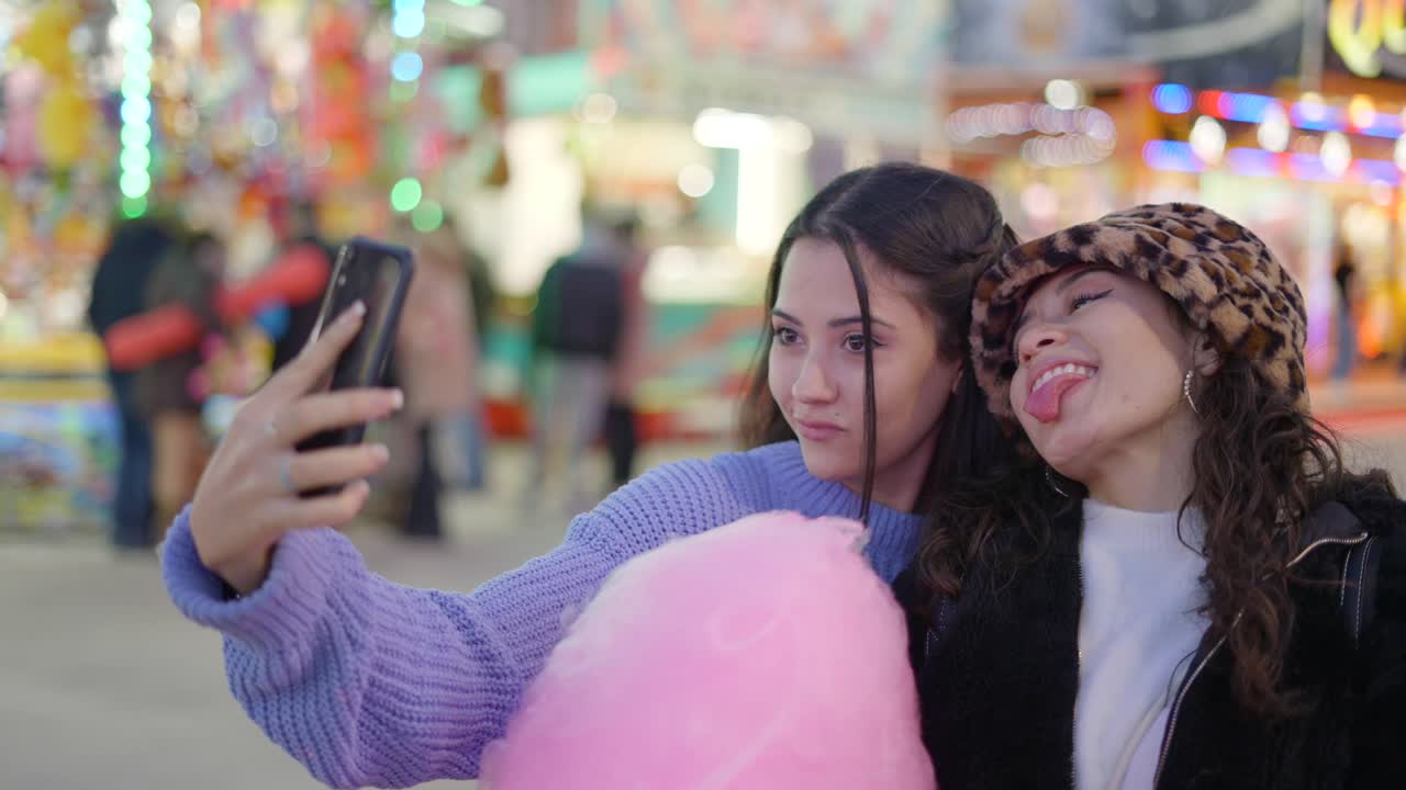 Two friends taking a selfie at a fun fair, enjoying cotton candy
