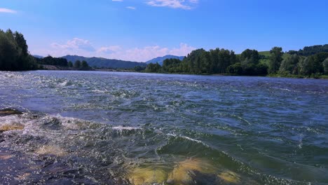 captivating river landscape: a serene view of flowing waters under a bright sky surrounded by lush greenery and majestic hills in the background