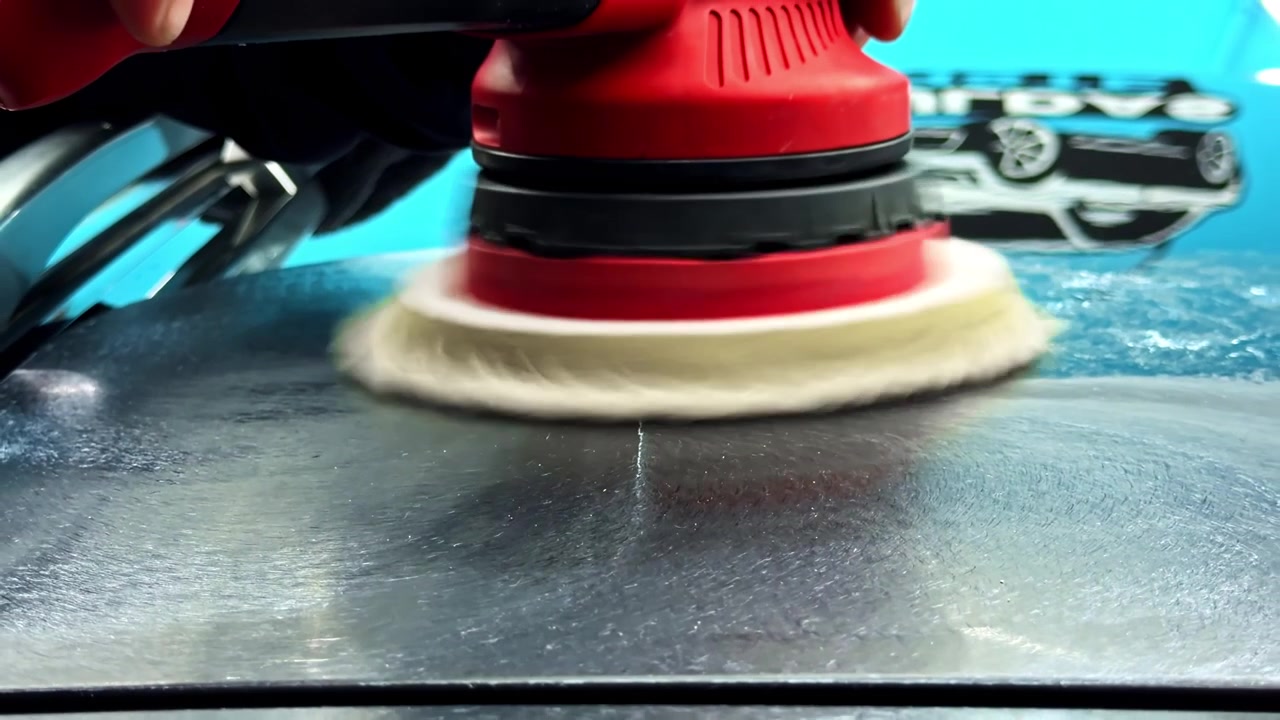 Primo piano di una lucidatrice rotativa che lucida un pannello nero di un'auto, mostrando la correzione della vernice, il miglioramento della lucentezza e il detailing auto professionale in azione.