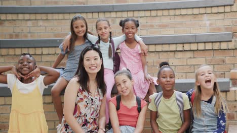 retrato de una feliz maestra diversa y escolares en las escaleras de una escuela primaria