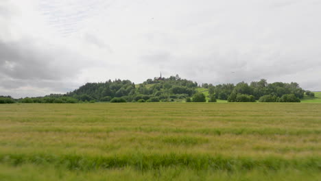 Drone-flying-over-long-grass-in-a-field-with-hill-backdrop-in-Europe