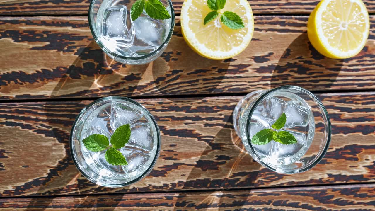 Top-down video shot of refreshing drinks with mint and ice on a rustic wooden table, accompanied