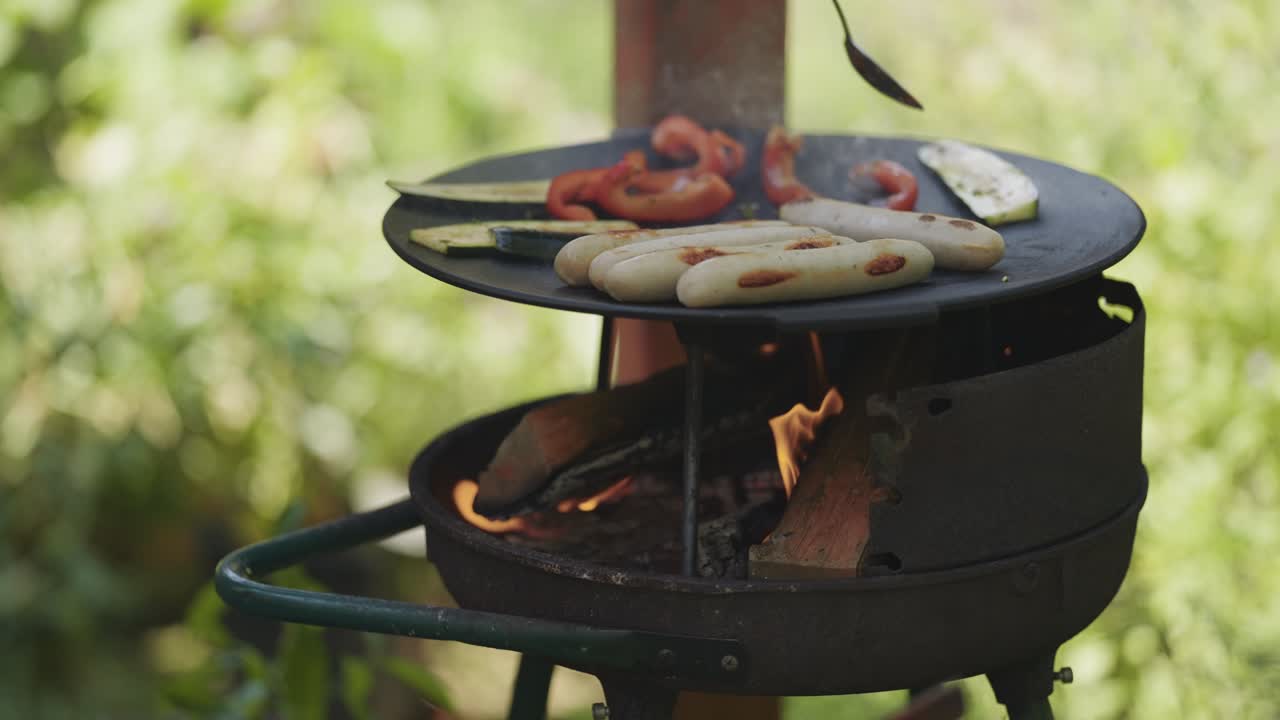 Verdure e salsicce vengono cotte sulla griglia in ghisa su un fuoco aperto all'aperto.