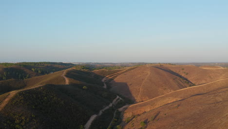 Aerial-forward-shot-of-beautiful-valley-surrounded-by-barren-hills-and-dirt-trails-in-Algarve,-Portugal