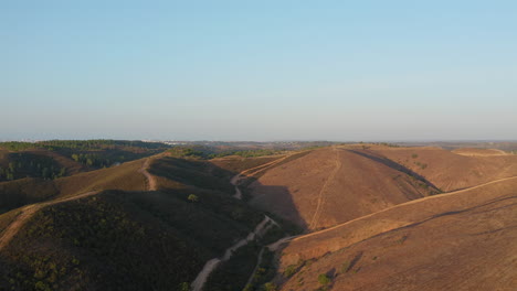 aerial forward shot of beautiful valley surrounded by barren hills and dirt trails in algarve, portugal