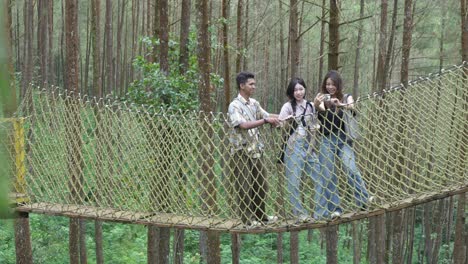 asian friends taking selfie on forest rope bridge in indonesia