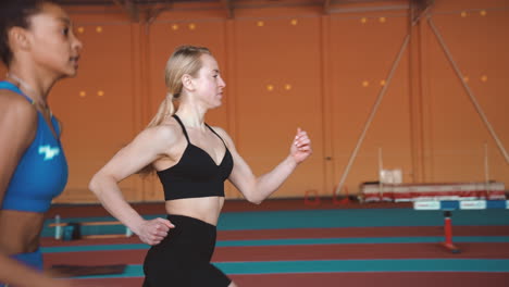 side view of two multiethnic female athletes running together on an indoor track