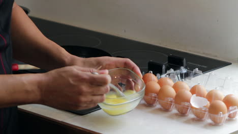 Beating-eggs-in-a-glass-bowl-on-kitchen-counter-near-stove-top-in-kitchen