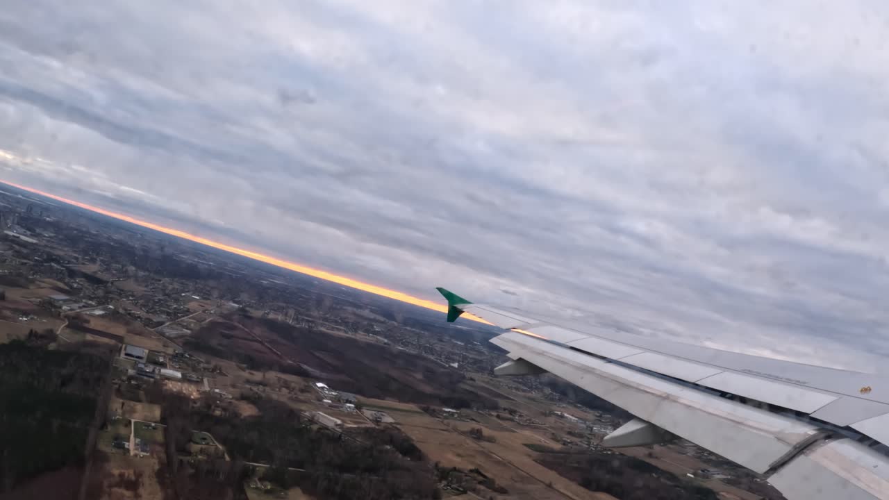 Airplane taking off, wing gliding over Riga, Latvia at sunset during a flight to Munich, Germany, capturing the warm colors of the sky and detailed landscape below