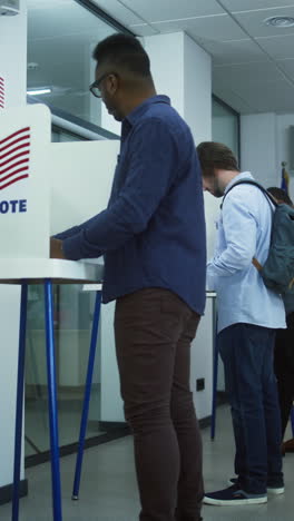 Dolly-shot-of-diverse-American-citizens-voting-in-booths-in-polling-station-office.-National-Election-Day-in-the-United-States.-Political-races-of-US-presidential-candidates.-Concept-of-civic-duty.