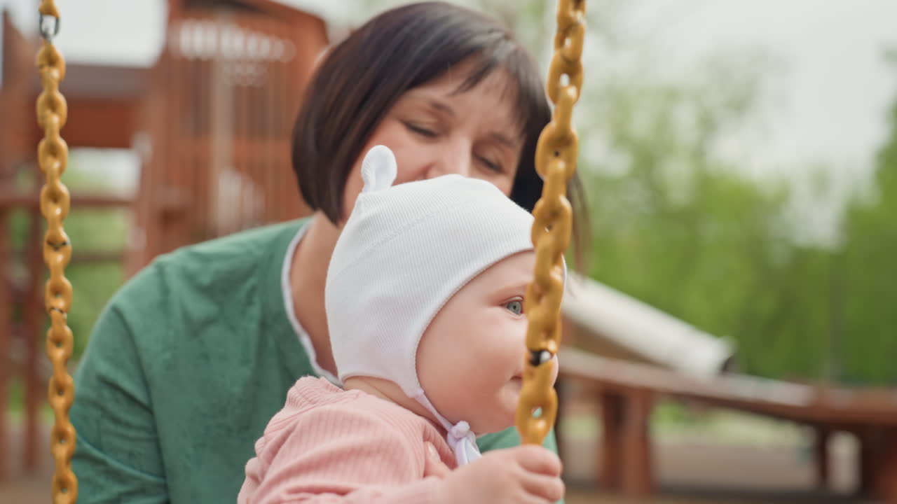 Inquisitive Infant Seated On Playground Swing, Thoughtful Young Child Resting On Hanging Playground Seat, Young Child Gazing Thoughtfully While Seated On Swing In Park With Caregiver Close By